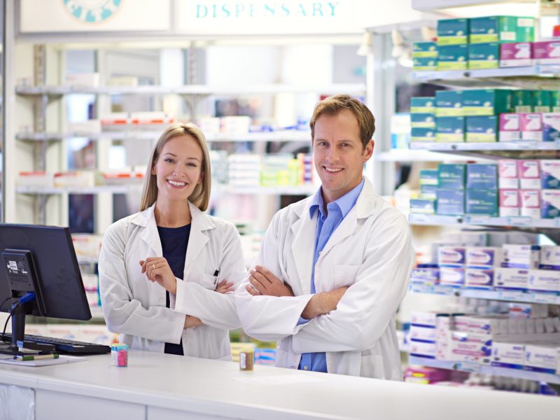 Portrait of two pharmacists standing at the prescription counter.